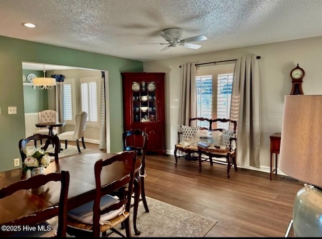 dining area with hardwood / wood-style floors, ceiling fan with notable chandelier, and a textured ceiling