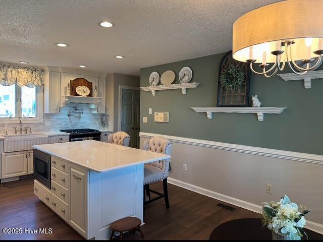 kitchen featuring a kitchen island, built in microwave, white cabinets, black gas stove, and dark wood-type flooring