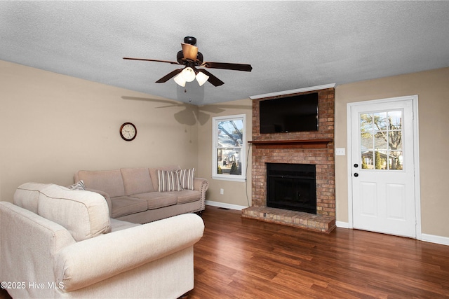 living room with ceiling fan, dark wood-type flooring, a textured ceiling, and a brick fireplace