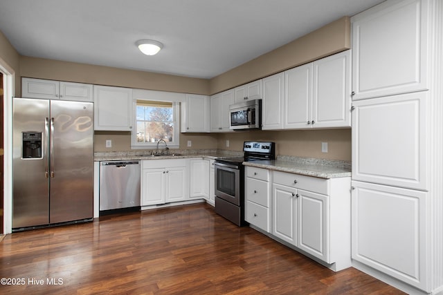 kitchen with light stone countertops, appliances with stainless steel finishes, white cabinets, sink, and dark wood-type flooring