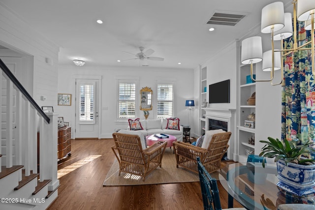 living room featuring hardwood / wood-style flooring, built in shelves, ceiling fan, and crown molding