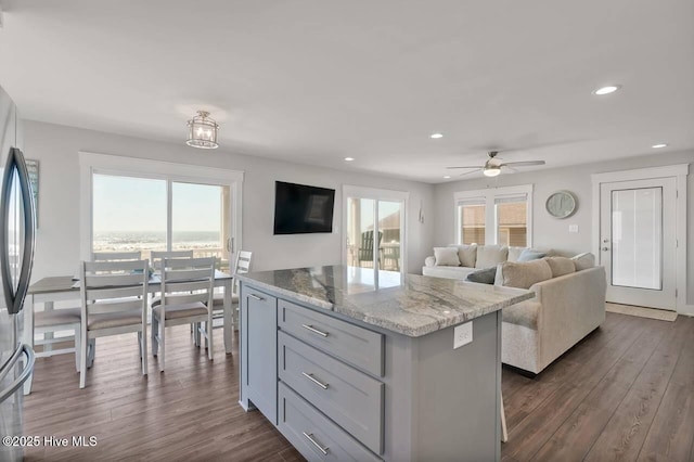 kitchen featuring light stone counters, ceiling fan, a wealth of natural light, a kitchen island, and dark wood-type flooring