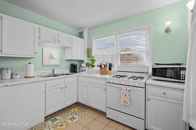 kitchen with white cabinets, white gas range, sink, and light tile patterned floors