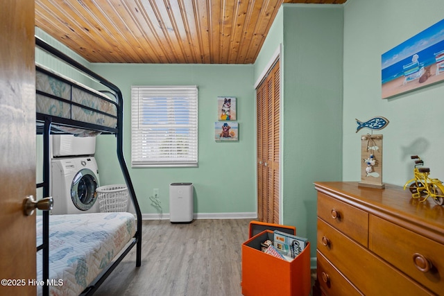 bedroom featuring stacked washer / dryer, wooden ceiling, light hardwood / wood-style flooring, and a closet