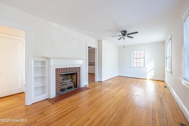 unfurnished living room with light wood-type flooring, a brick fireplace, built in shelves, and ceiling fan