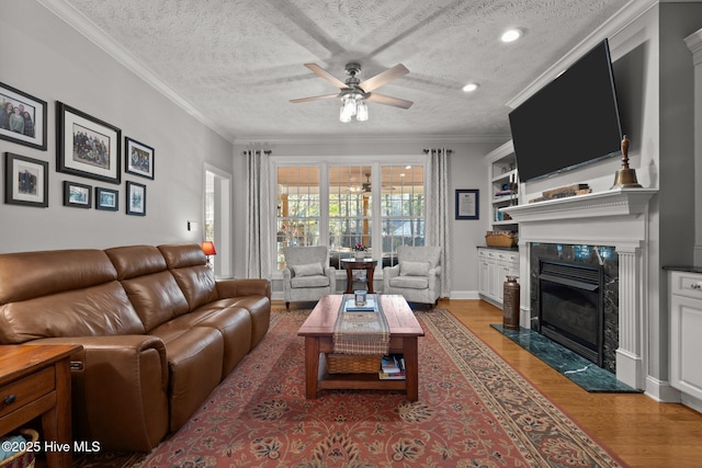 living room with ceiling fan, a high end fireplace, ornamental molding, a textured ceiling, and light wood-type flooring