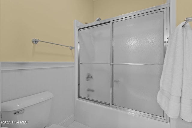 bathroom featuring toilet and bath / shower combo with glass door