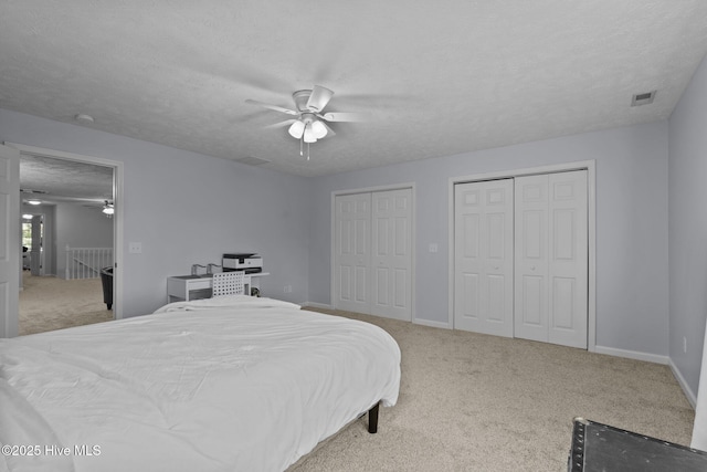 carpeted bedroom with a textured ceiling, two closets, and ceiling fan