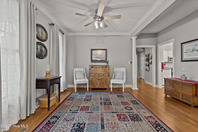 sitting room with hardwood / wood-style flooring, ceiling fan, ornate columns, and a textured ceiling