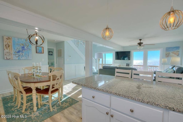 kitchen with light stone countertops, light hardwood / wood-style flooring, decorative light fixtures, white cabinets, and ceiling fan