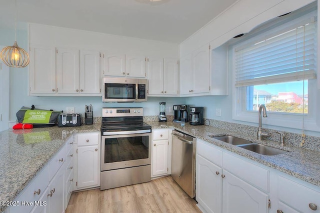 kitchen featuring sink, white cabinets, decorative light fixtures, light wood-type flooring, and appliances with stainless steel finishes