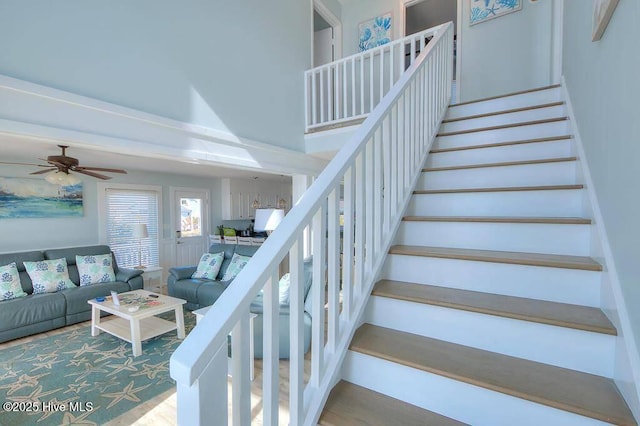 stairs with ceiling fan, a high ceiling, and wood-type flooring