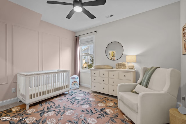 bedroom with ceiling fan, light carpet, and a nursery area