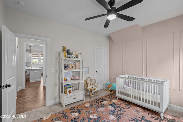 carpeted bedroom featuring ceiling fan, a crib, and sink