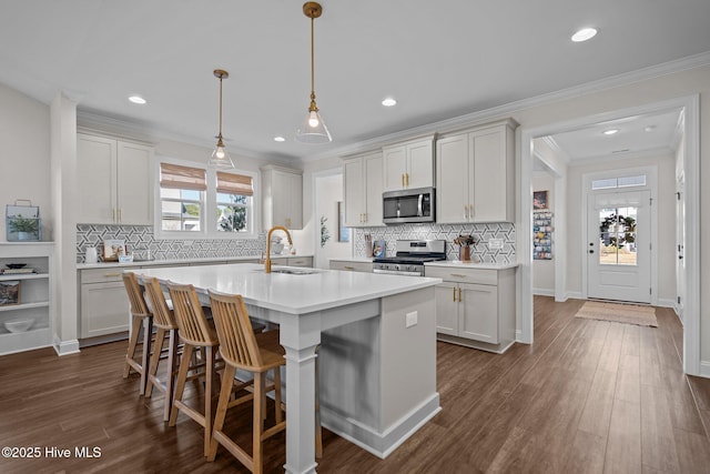 kitchen with appliances with stainless steel finishes, sink, pendant lighting, white cabinets, and an island with sink