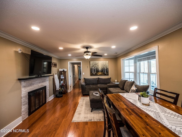 living room featuring a stone fireplace, ceiling fan, crown molding, and wood-type flooring