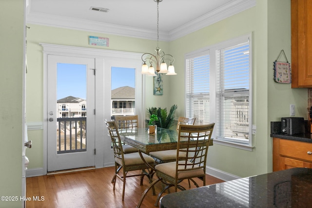 dining area with a chandelier, baseboards, wood finished floors, visible vents, and ornamental molding