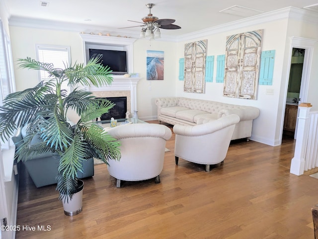 living room with a ceiling fan, wood finished floors, baseboards, a glass covered fireplace, and ornamental molding