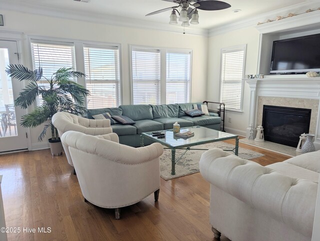 living room with crown molding, a fireplace, a ceiling fan, baseboards, and wood finished floors