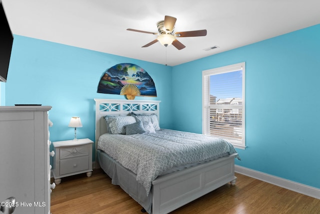 bedroom featuring visible vents, a ceiling fan, baseboards, and wood finished floors