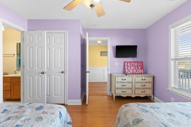 bedroom featuring a ceiling fan, baseboards, wood finished floors, ensuite bathroom, and a closet