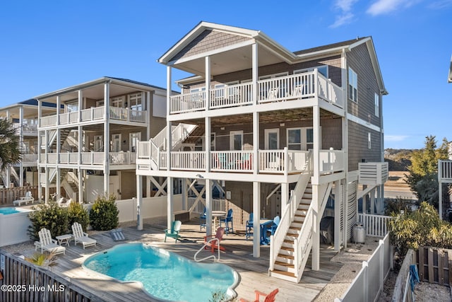back of property with stairs, a fenced backyard, a wooden deck, and a fenced in pool