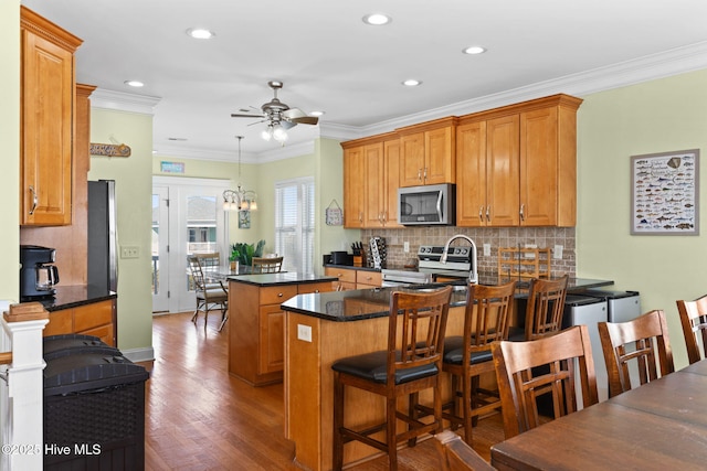 kitchen featuring a peninsula, a kitchen island, tasteful backsplash, a ceiling fan, and stainless steel appliances