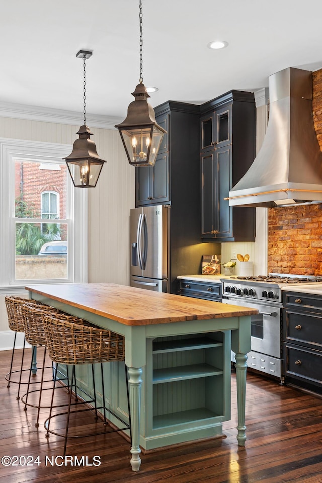 kitchen with a kitchen breakfast bar, appliances with stainless steel finishes, decorative light fixtures, wall chimney range hood, and wood counters