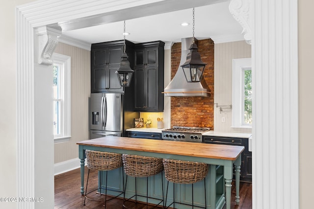 kitchen with wall chimney exhaust hood, stainless steel refrigerator with ice dispenser, butcher block counters, ornamental molding, and stove