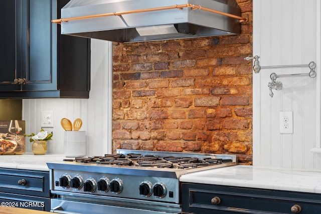 kitchen featuring stainless steel range, brick wall, and light stone countertops