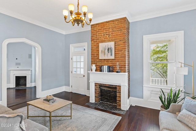 living room with an inviting chandelier, a brick fireplace, ornamental molding, and dark hardwood / wood-style flooring