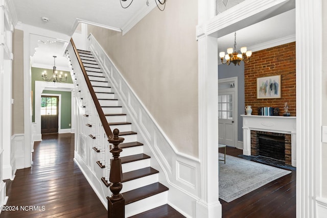 stairs featuring a brick fireplace, an inviting chandelier, hardwood / wood-style floors, and crown molding