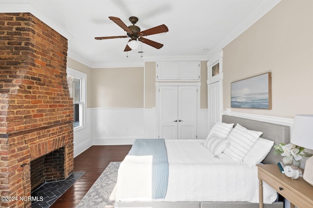 bedroom with dark wood-style flooring, ornamental molding, a closet, wainscoting, and a brick fireplace