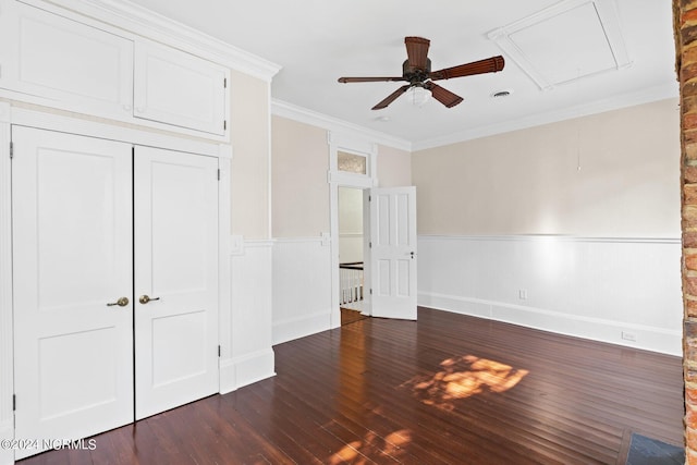 unfurnished bedroom featuring attic access, dark wood-style floors, crown molding, and a wainscoted wall