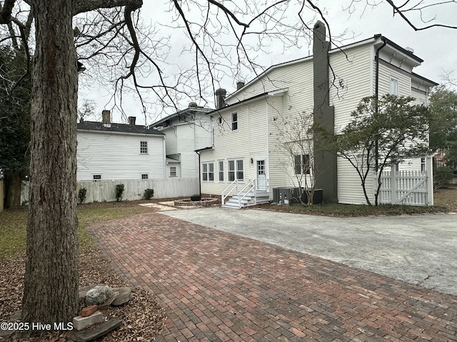 rear view of house featuring central air condition unit, a chimney, and fence