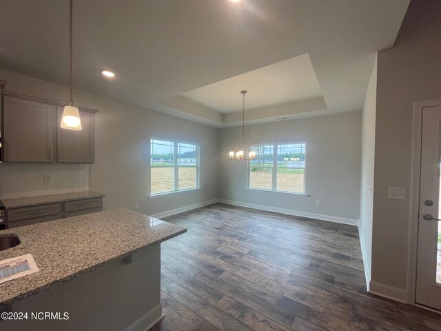 kitchen featuring light stone counters, a tray ceiling, pendant lighting, a notable chandelier, and dark hardwood / wood-style floors