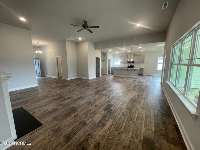 unfurnished living room with dark wood-type flooring and ceiling fan with notable chandelier