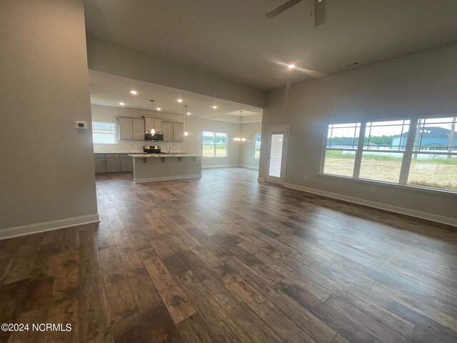 unfurnished living room featuring dark hardwood / wood-style floors, sink, and ceiling fan with notable chandelier