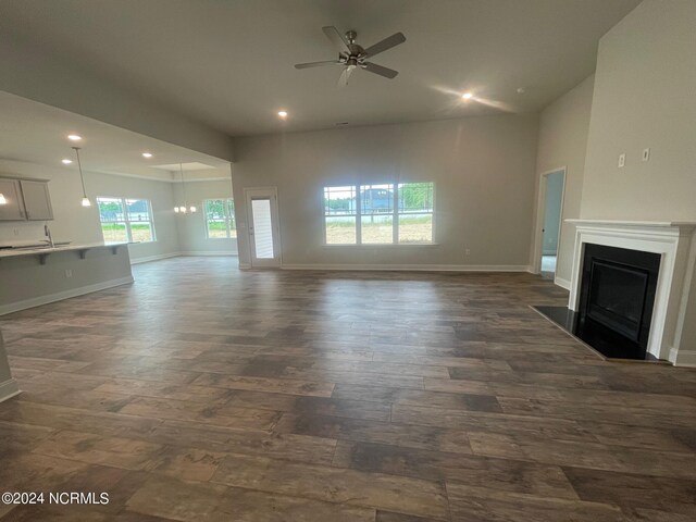 unfurnished living room with sink, dark wood-type flooring, and ceiling fan with notable chandelier