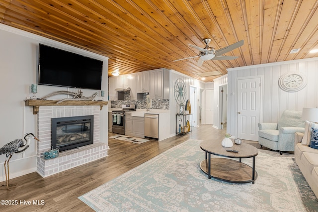 living room featuring wooden ceiling, a fireplace, ceiling fan, wood-type flooring, and crown molding