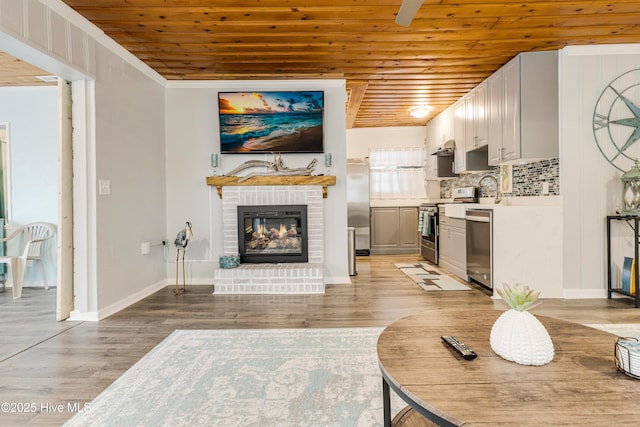 living room with wood ceiling, light wood-type flooring, crown molding, and a fireplace