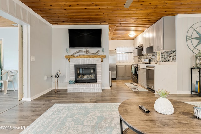 living room featuring wooden ceiling, light wood-type flooring, crown molding, a fireplace, and sink