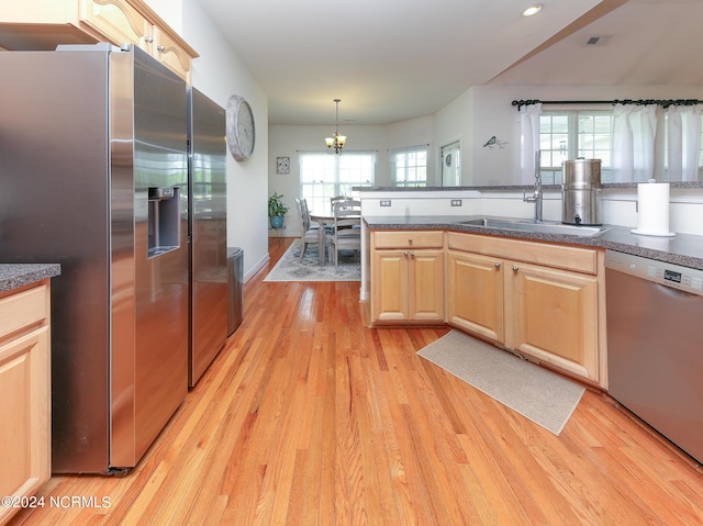 kitchen with light brown cabinets, a sink, hanging light fixtures, appliances with stainless steel finishes, and dark countertops