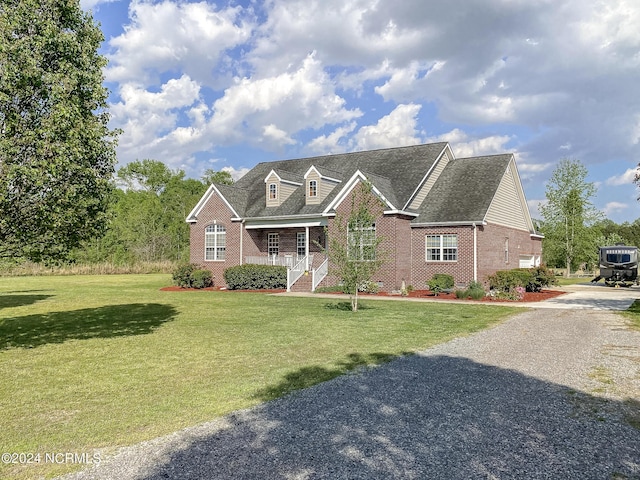 view of front of property with covered porch, brick siding, gravel driveway, and a front yard