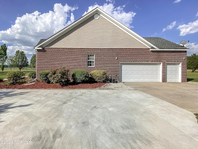 view of side of home with a shingled roof, concrete driveway, brick siding, and an attached garage