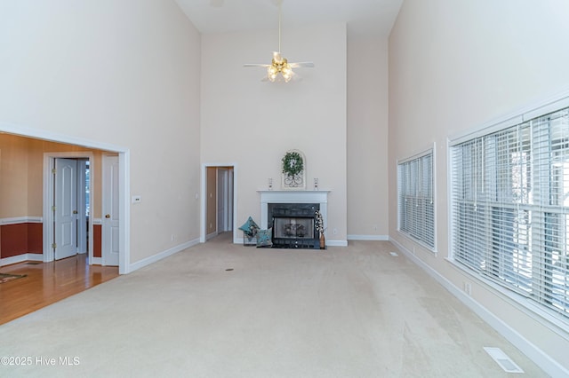 unfurnished living room with a towering ceiling, light colored carpet, and ceiling fan