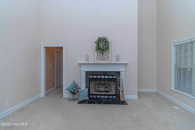 unfurnished living room featuring a fireplace, a towering ceiling, and light colored carpet