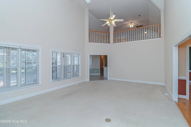 unfurnished living room featuring ceiling fan, high vaulted ceiling, a healthy amount of sunlight, and light colored carpet