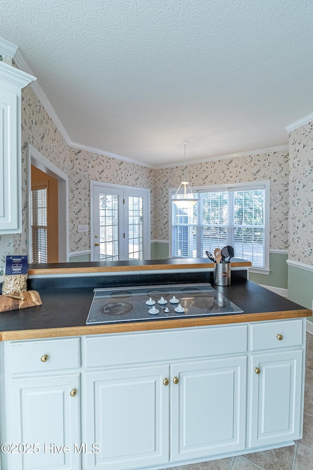 kitchen featuring stovetop, a textured ceiling, white cabinetry, and crown molding