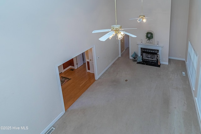 living room with ceiling fan, light colored carpet, and a high ceiling